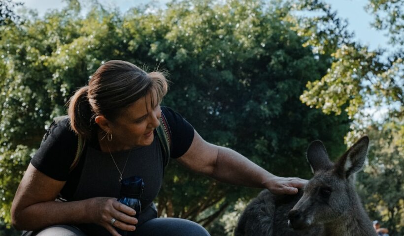 woman in black t-shirt sitting beside gray kangaroo during daytime