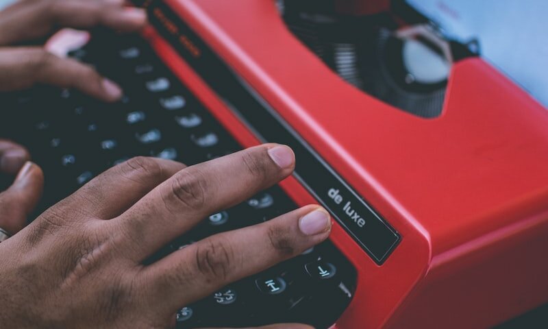 person typing on red typewriter