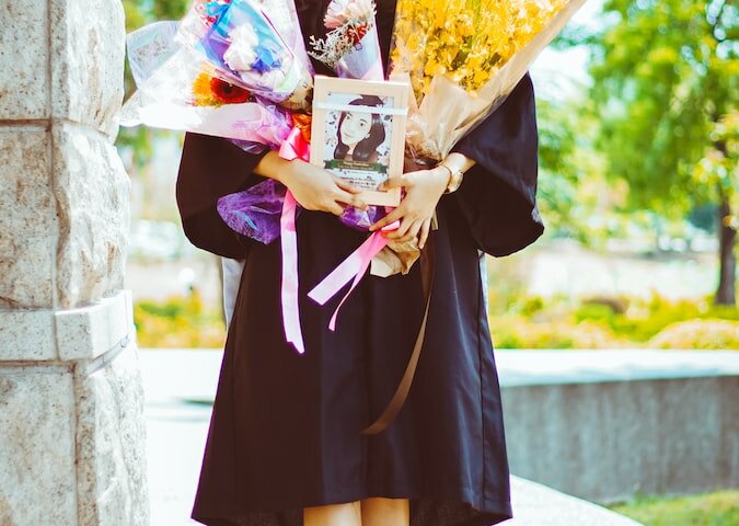 woman in black and purple academic dress holding bouquet of flowers